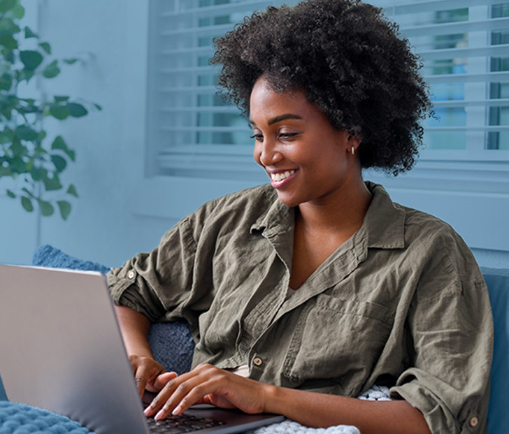A smiling woman sitting on a couch at home working on a laptop computer