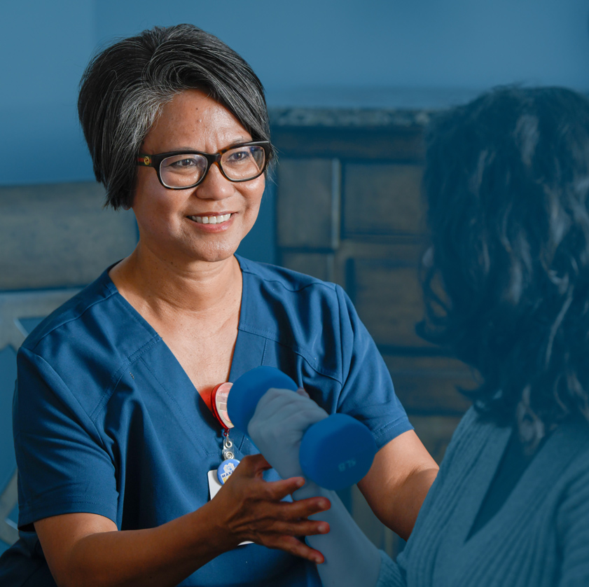 A smiling female physical therapist helping a patient lift a weight