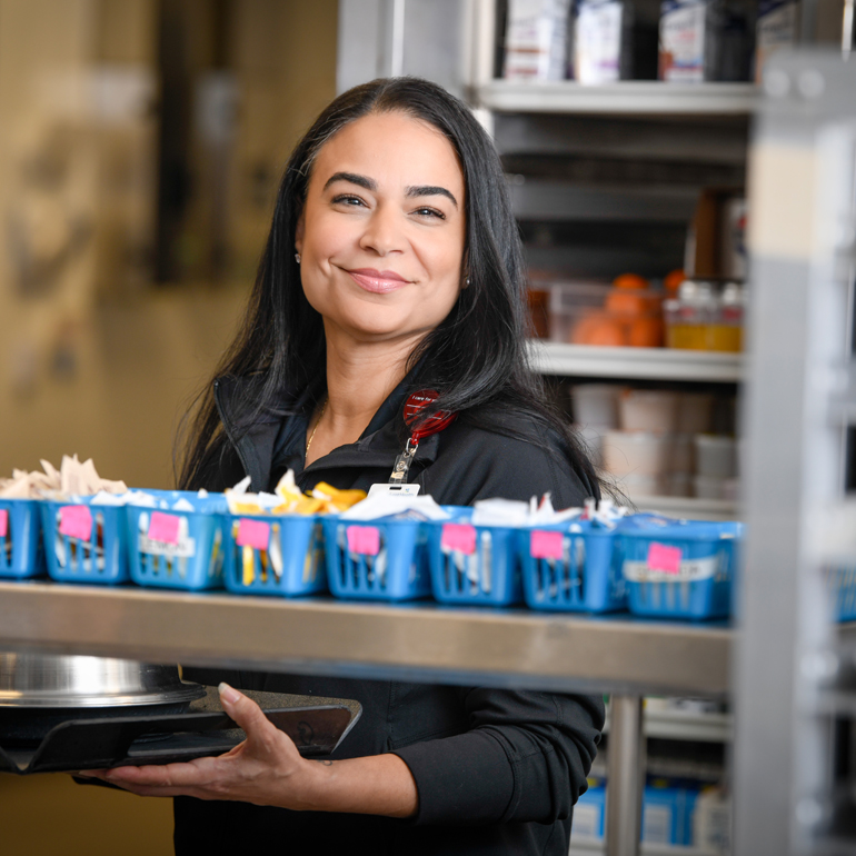 A smiling female nutrition services worker holding a tray