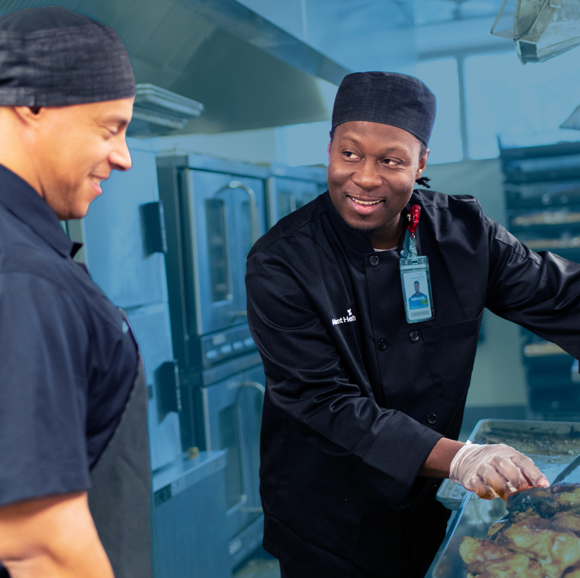 Two male nutritional services workers in a kitchen environment