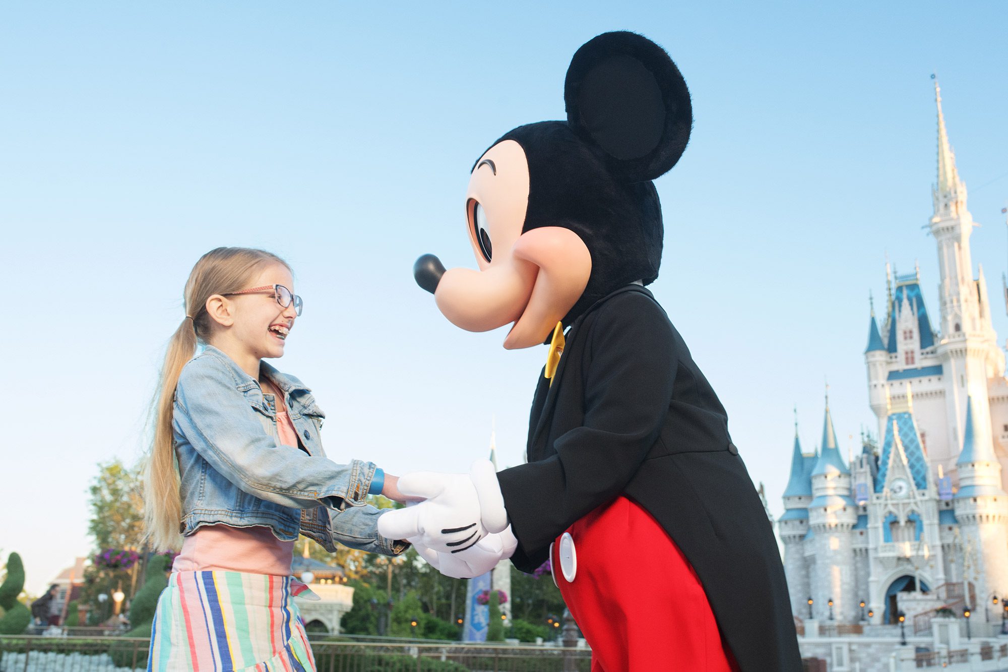 Mickey Mouse holding a girls hands in front of Cinderella's Castle.