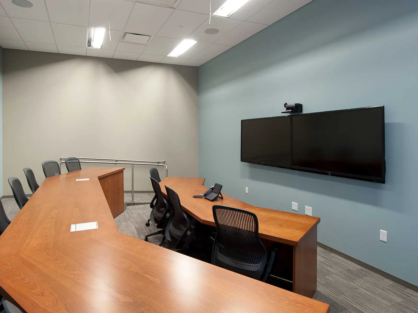 A meeting room where a wide screen tv, with a webcam, is pointing at two vertical-aligned tables.