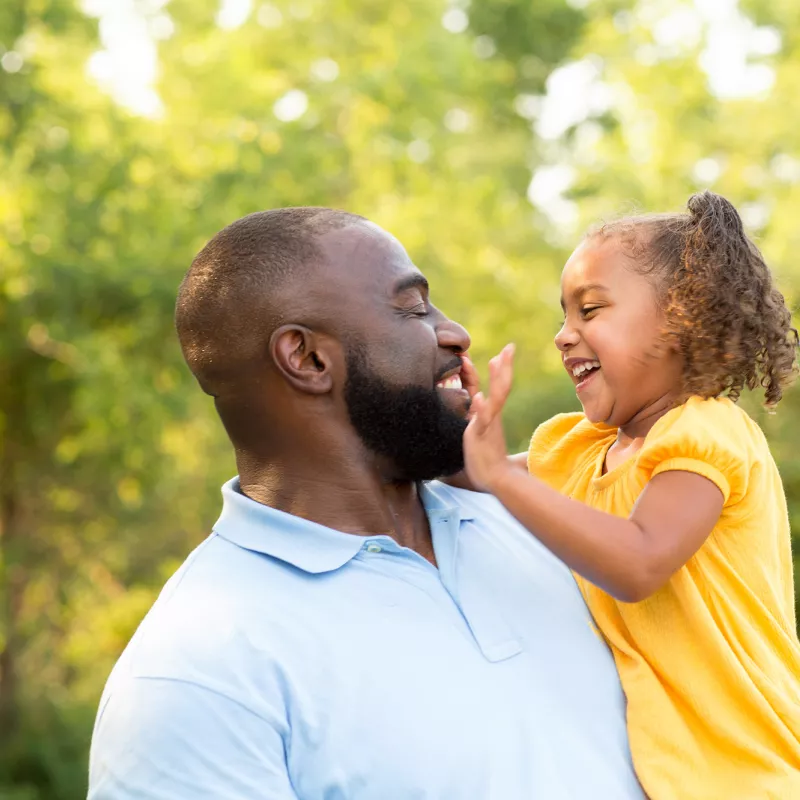 African-American father holding his African-American daughter with her hand in his face while in the forest