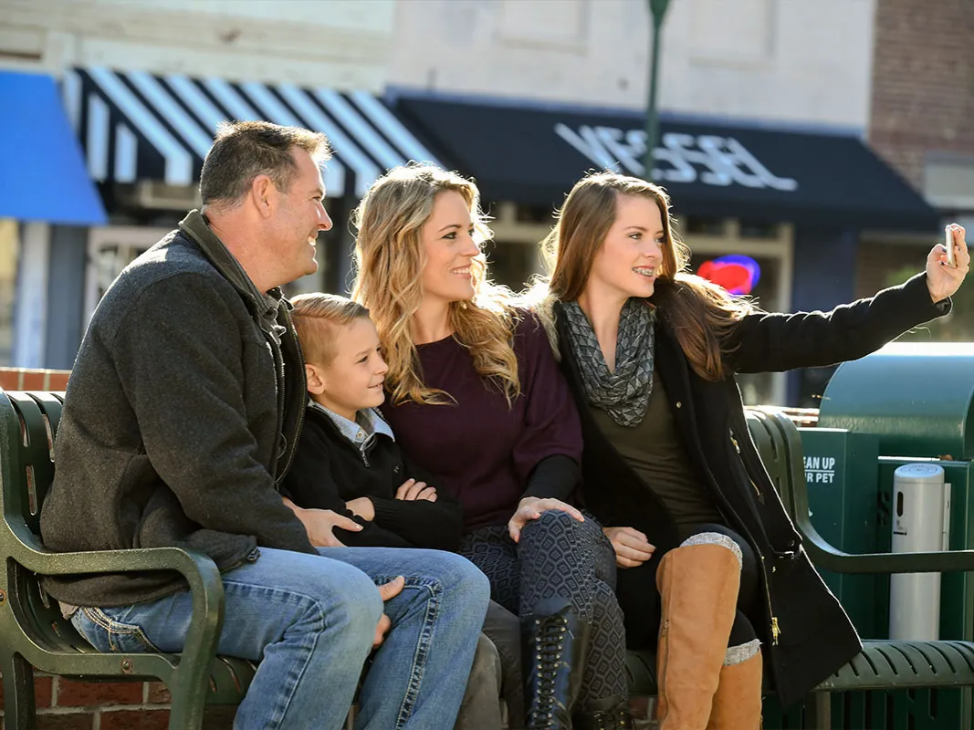 Family sitting on a park bench taking a selfie photo