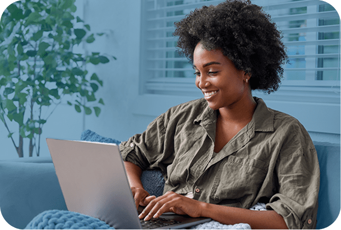 A smiling woman sitting on a couch in her living room and working on a laptop computer