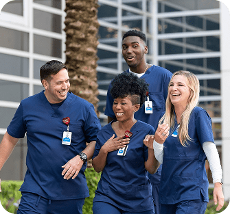 Four smiling and laughing healthcare professionals walking outside of an AdventHealth healthcare facility