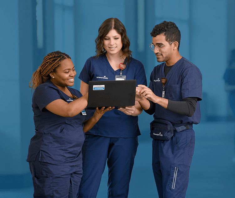 Three healthcare professionals standing together and collaborating in front of a laptop computer