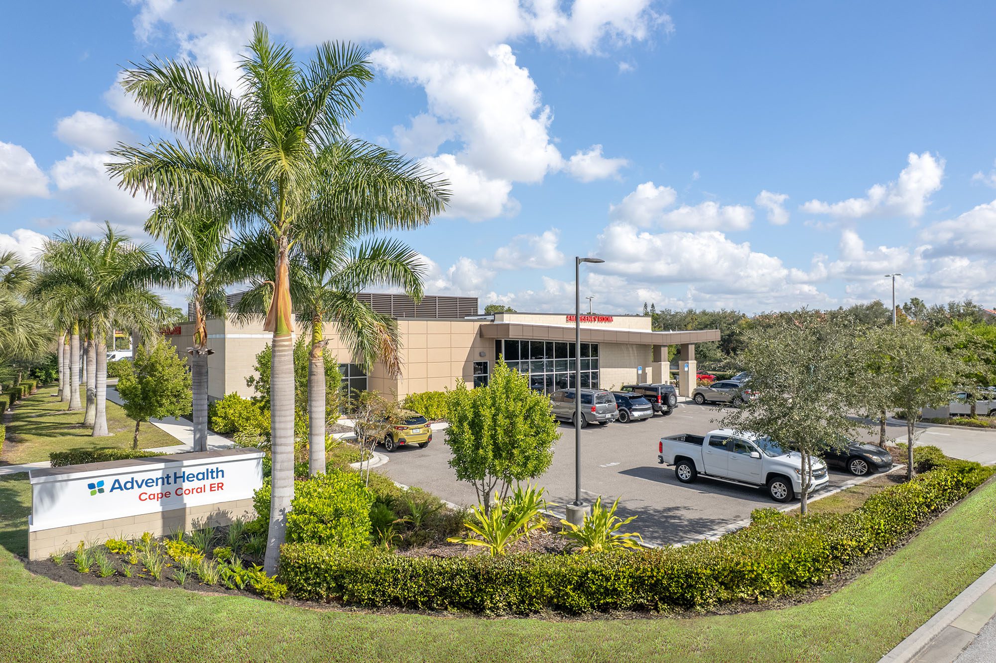AdventHealth Cape Coral ER building with palm trees and parking lot under a blue sky.