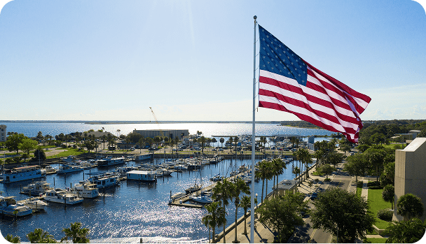 Large American flag flying over moored ships in an Orlando marina with the ocean and horizon in the background