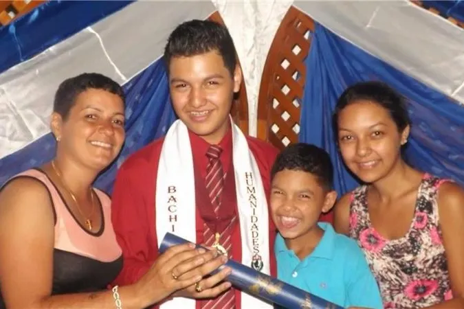 Young graduate holding a diploma and posing with three family members.