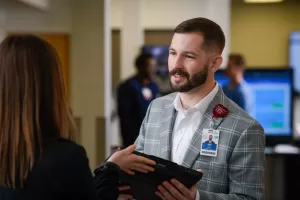 Team member speaking with a colleague while holding a tablet in a hospital setting.